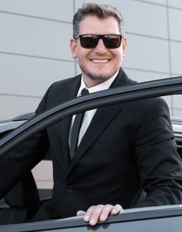 Smiling man wearing sunglasses beside an open dark car door
