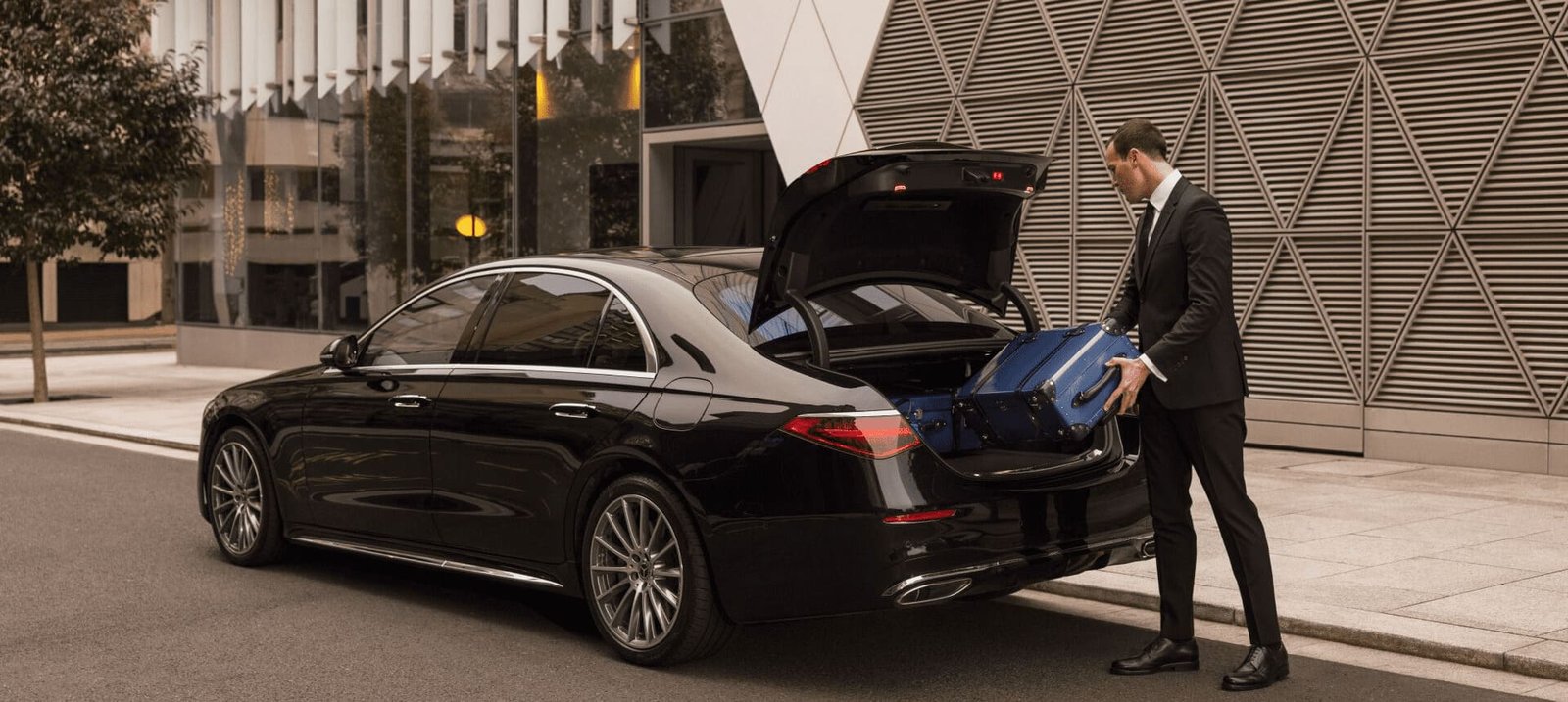 Man placing a bag in the open boot of a black saloon outside a building