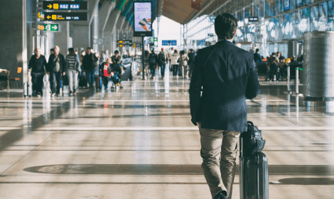 Traveller seen from behind pulling a suitcase through a bright terminal