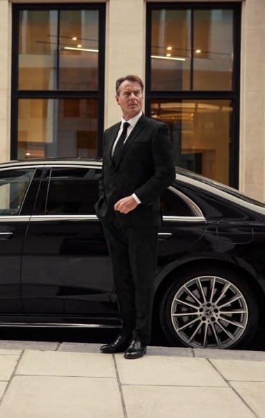 Suited attendant standing beside a black saloon outside a building entrance