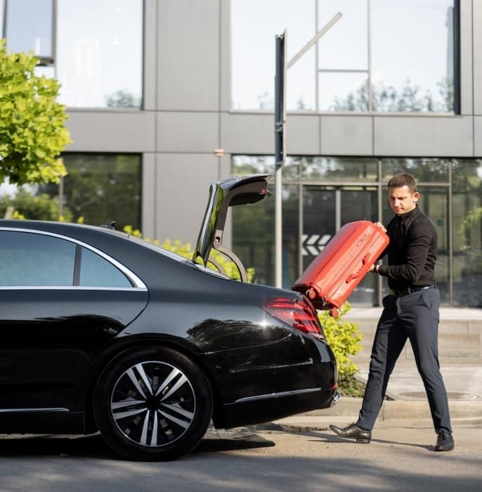 Man lifting an orange suitcase beside the open boot of a black saloon