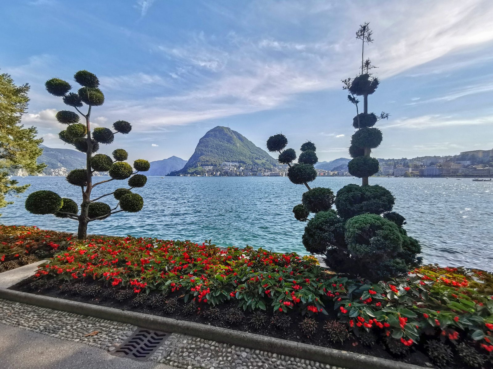 Lugano lakefront flowerbeds and sculpted trees facing Monte San Salvatore