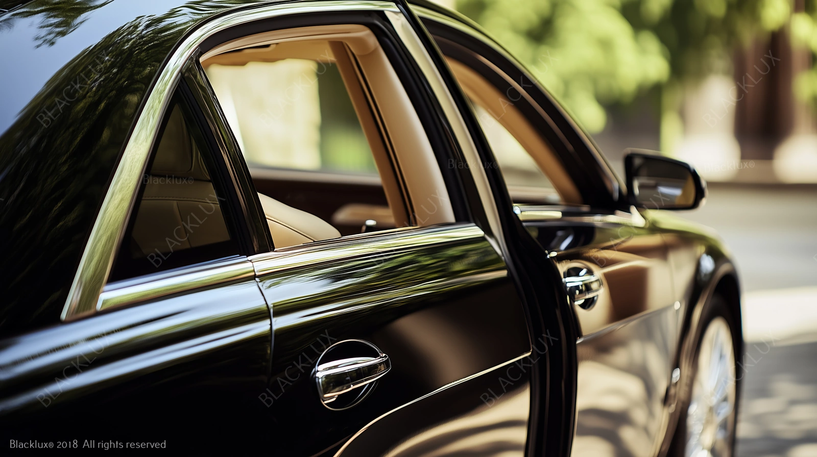 Open rear door of a black saloon with greenery reflected in the bodywork
