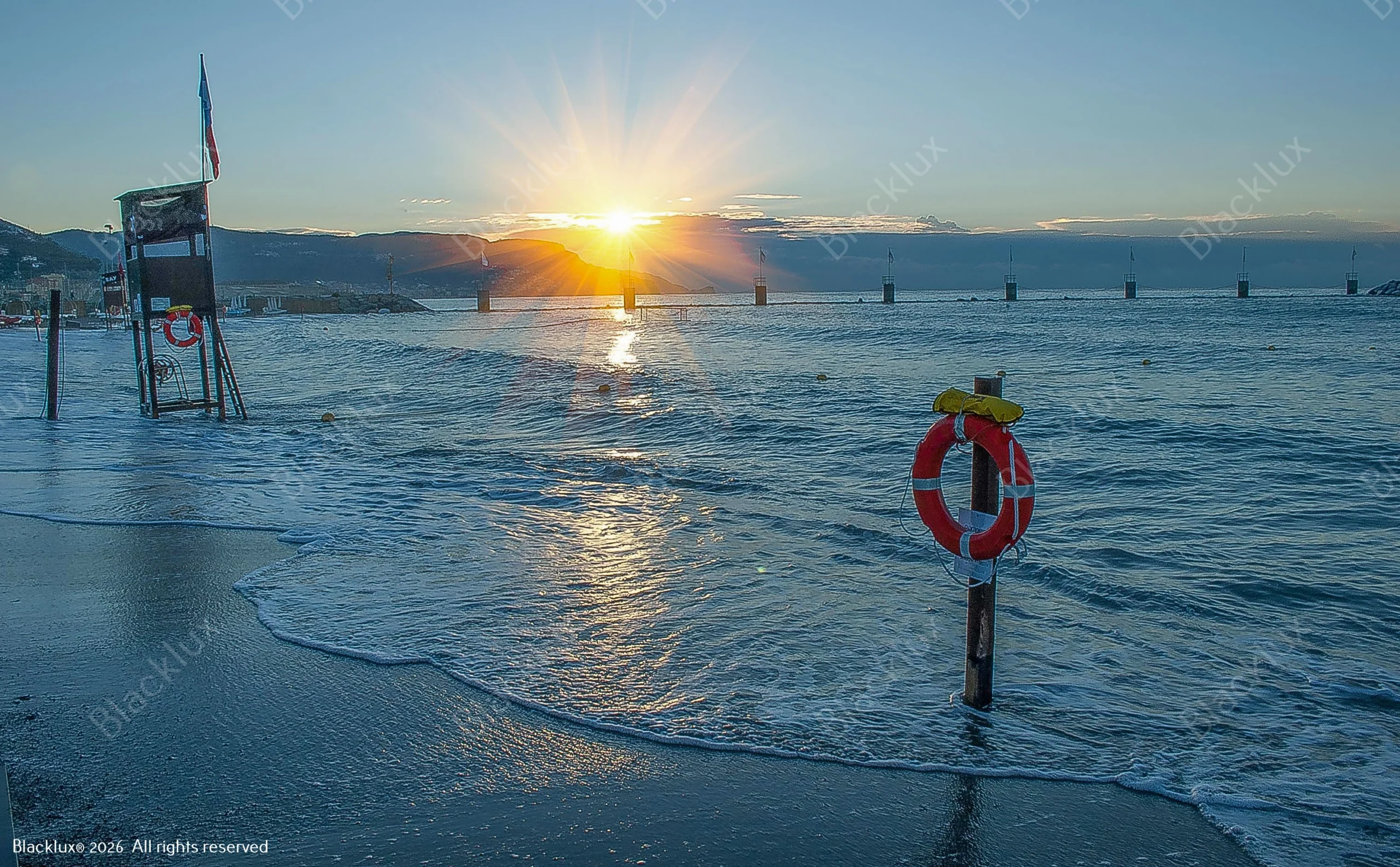 Lifebuoy beside calm coastal water with a low golden sun and hills on the horizon