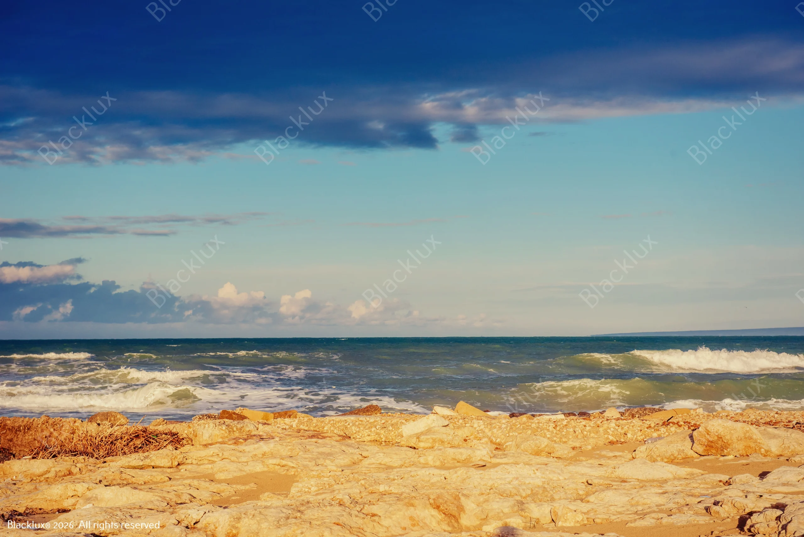 Rocky shoreline with golden stones and blue water under soft coastal light