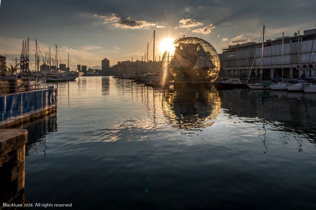 Genoa Porto Antico at sunset with the glass Biosfera, moored boats and reflections