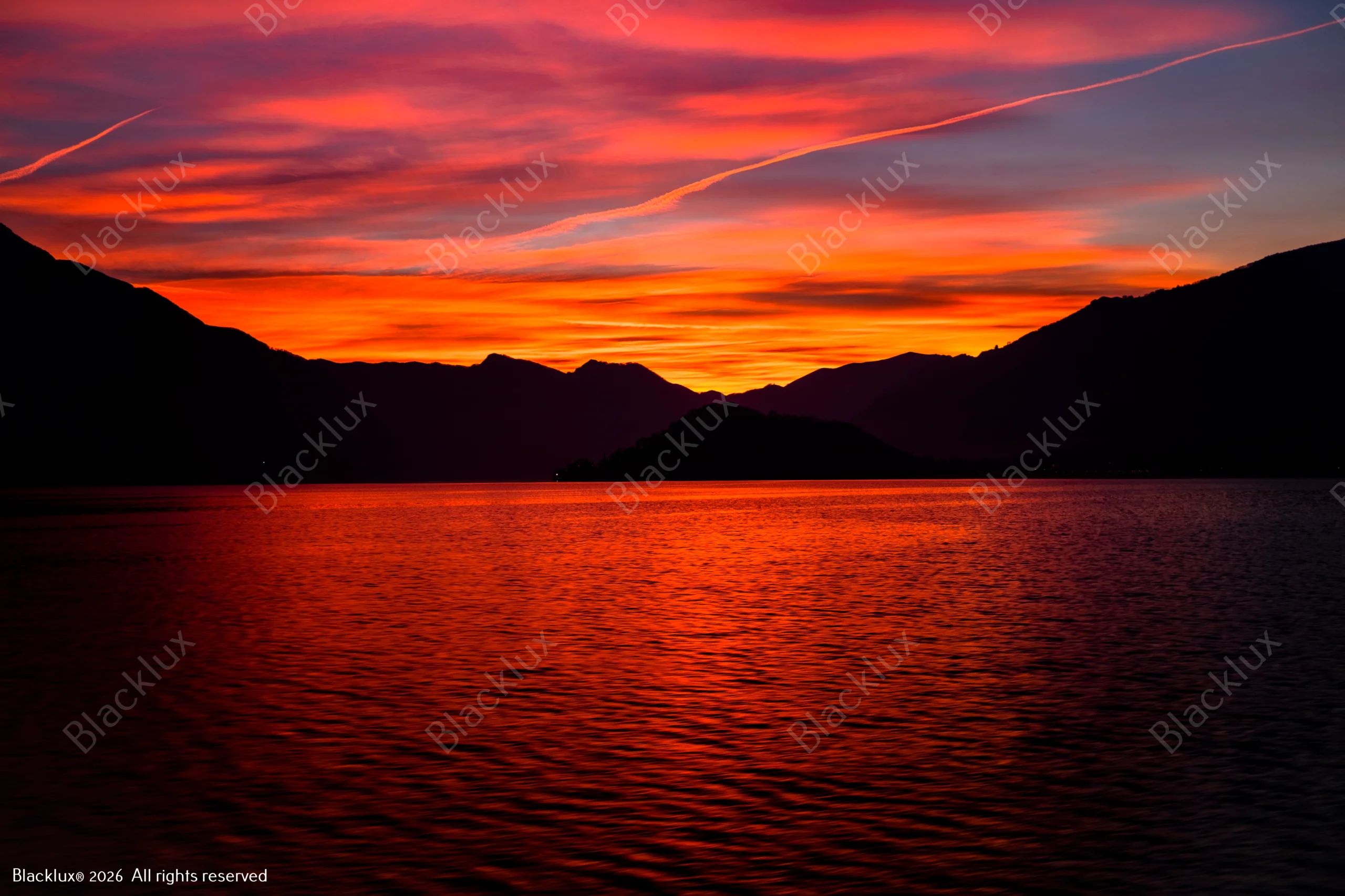 Red-orange sunset reflected on a lake between dark mountain silhouettes