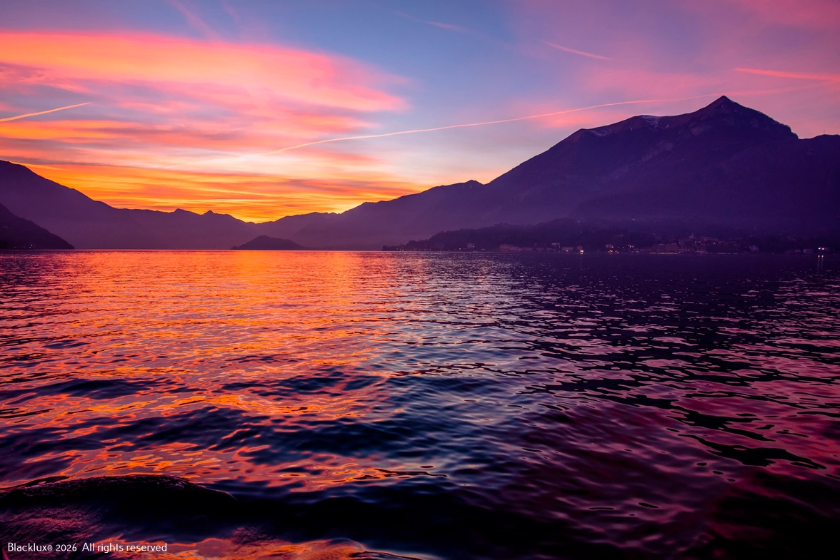 Pink and orange sunset reflected across a lake between dark hills