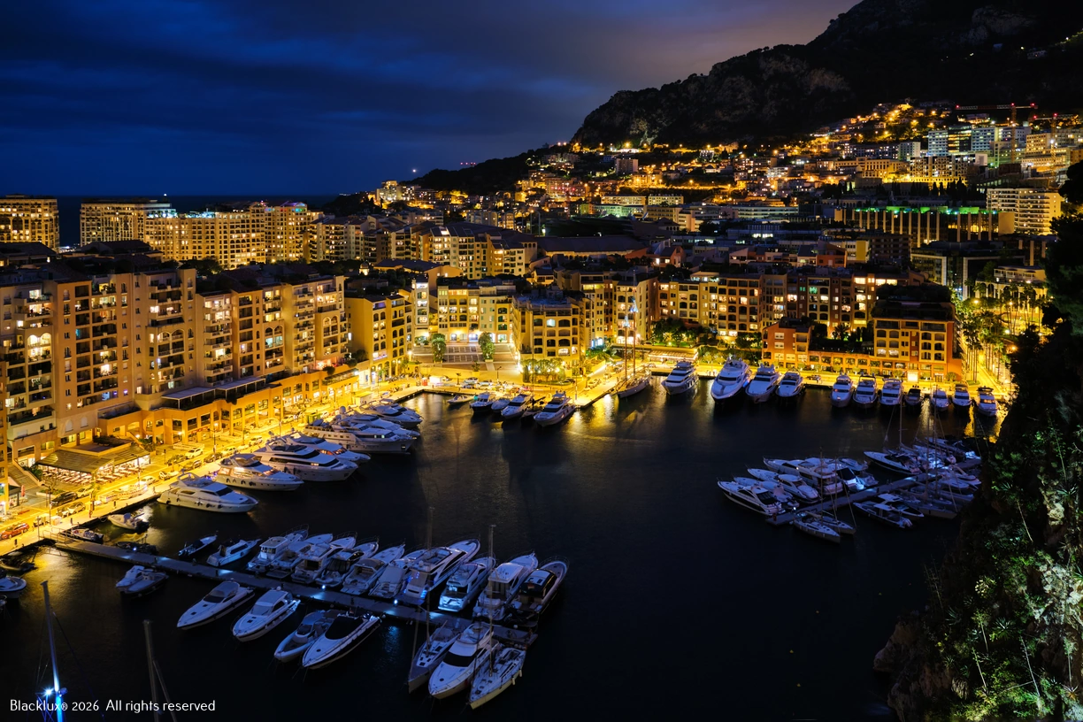 Elevated evening view of Monaco harbour with yachts and illuminated waterfront buildings
