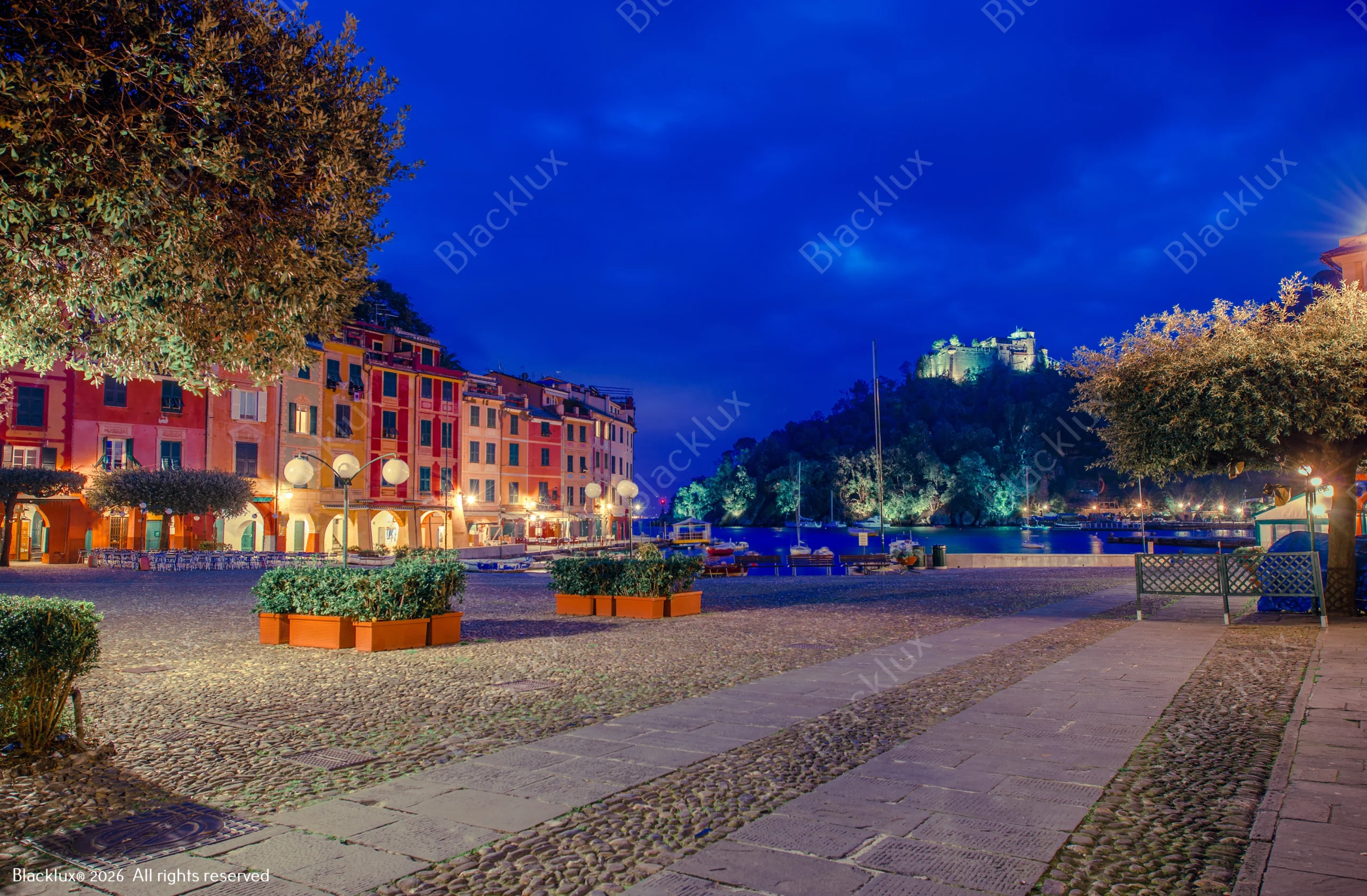 Wide paved waterfront square with illuminated colourful buildings at dusk