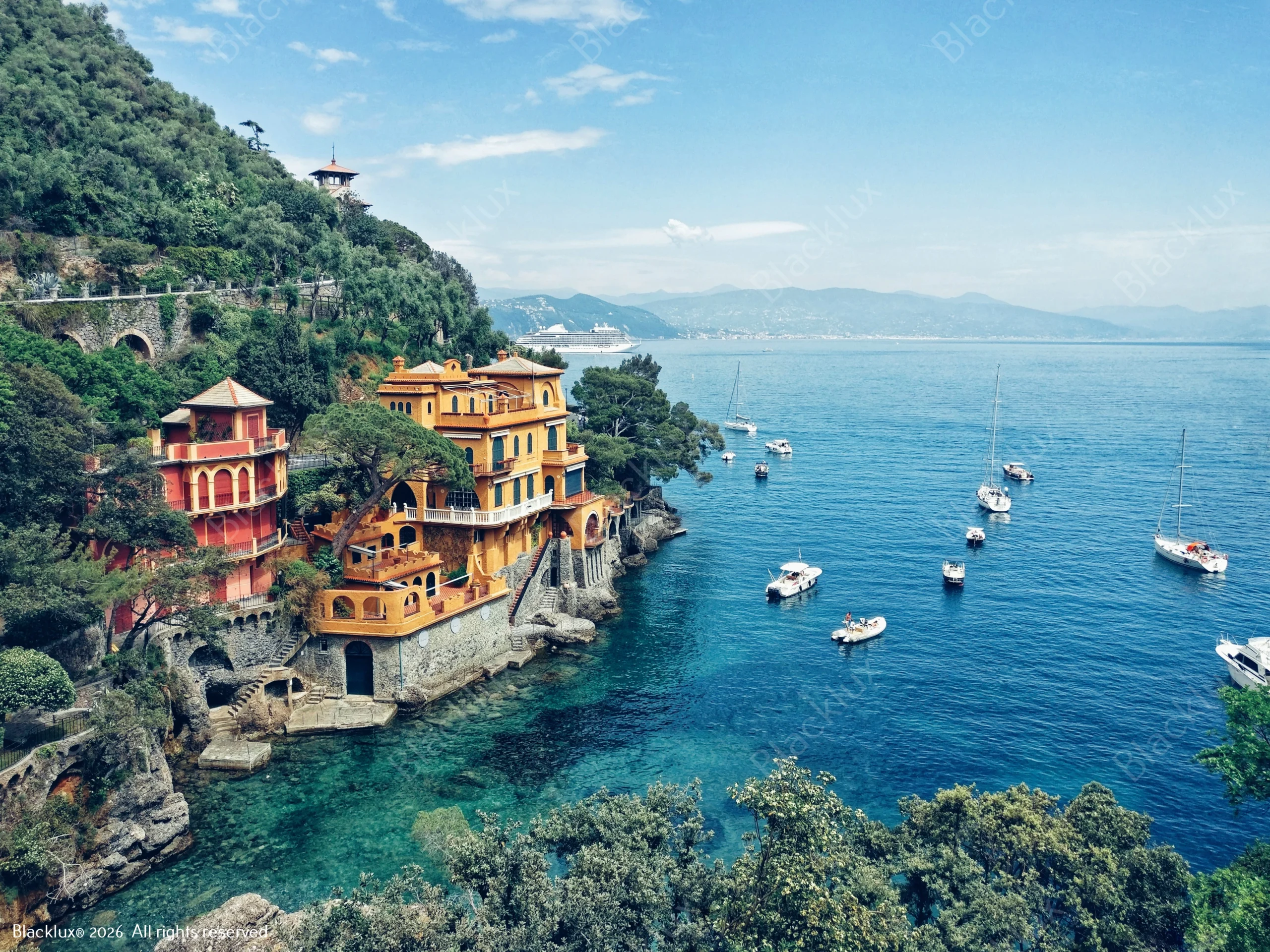 Colourful villas above a turquoise Riviera cove with moored boats and a wooded slope