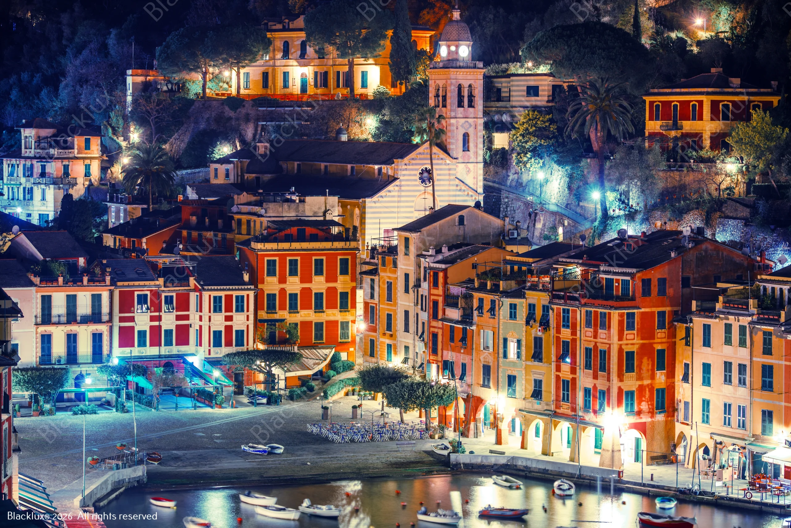 Illuminated Portofino waterfront buildings and church seen across the harbour at night