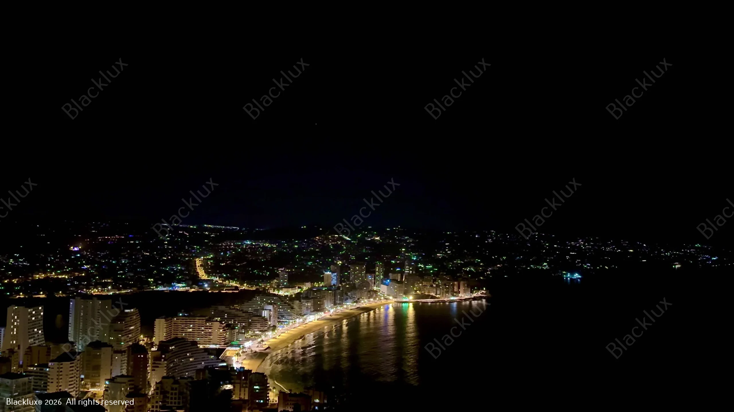Long curve of coastal lights viewed above a dark bay at night
