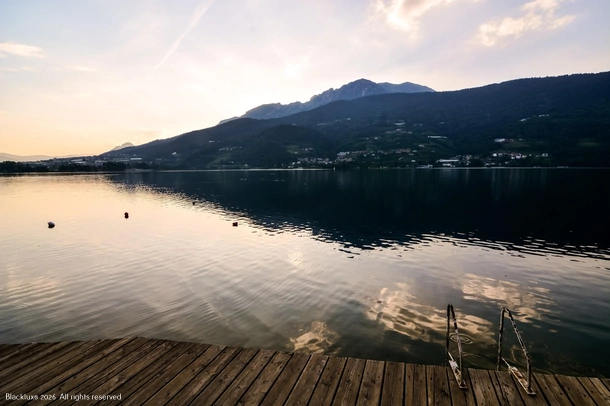 Wooden lakeside pontoon with a metal ladder, calm water and mountain reflections at dusk