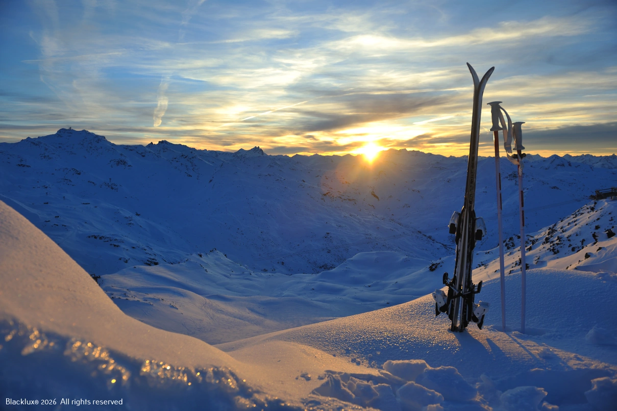 Aufrecht stehende Ski vor verschneiten Bergen bei Sonnenuntergang