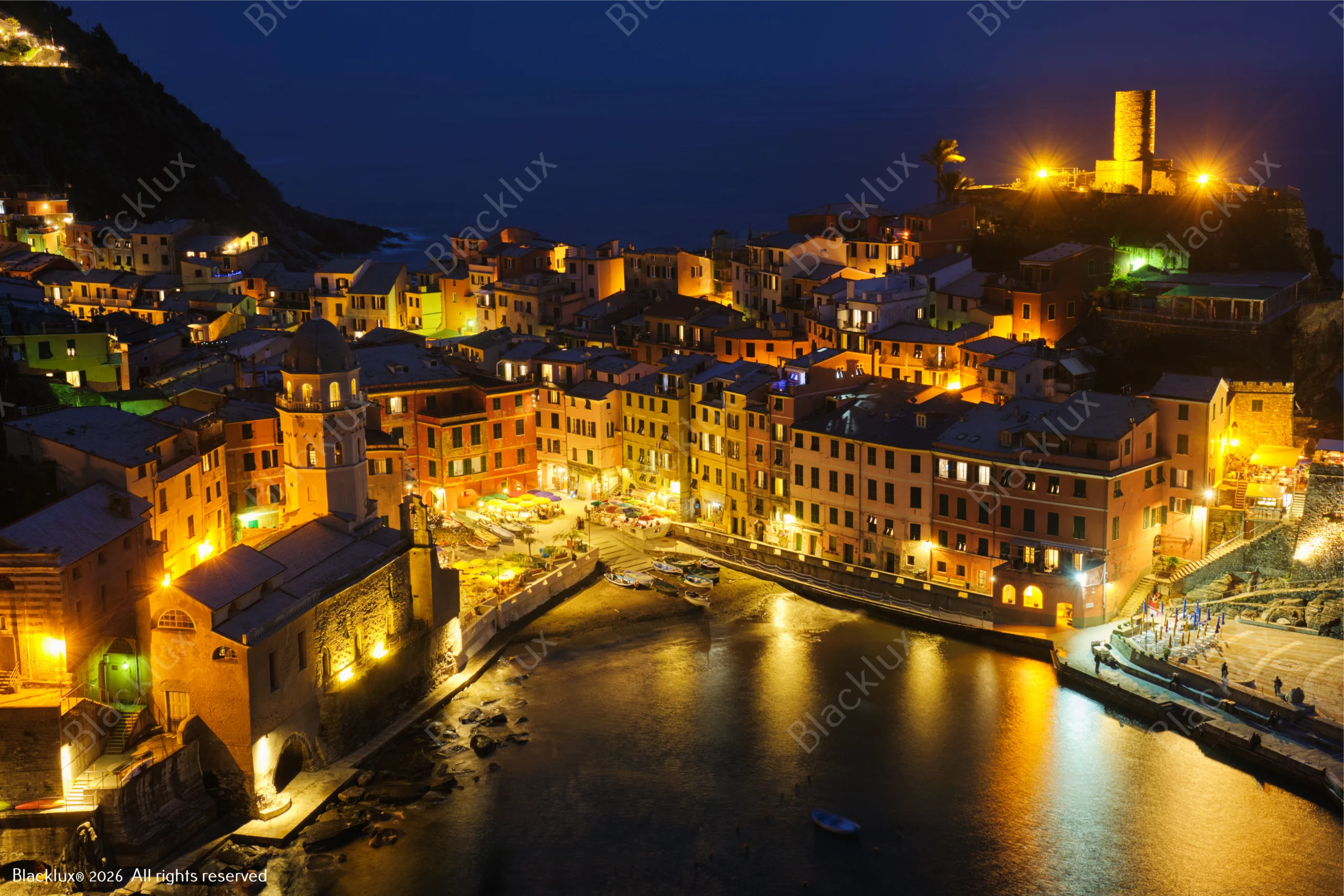 Night panorama of Vernazza with illuminated waterfront buildings, church square and castle tower