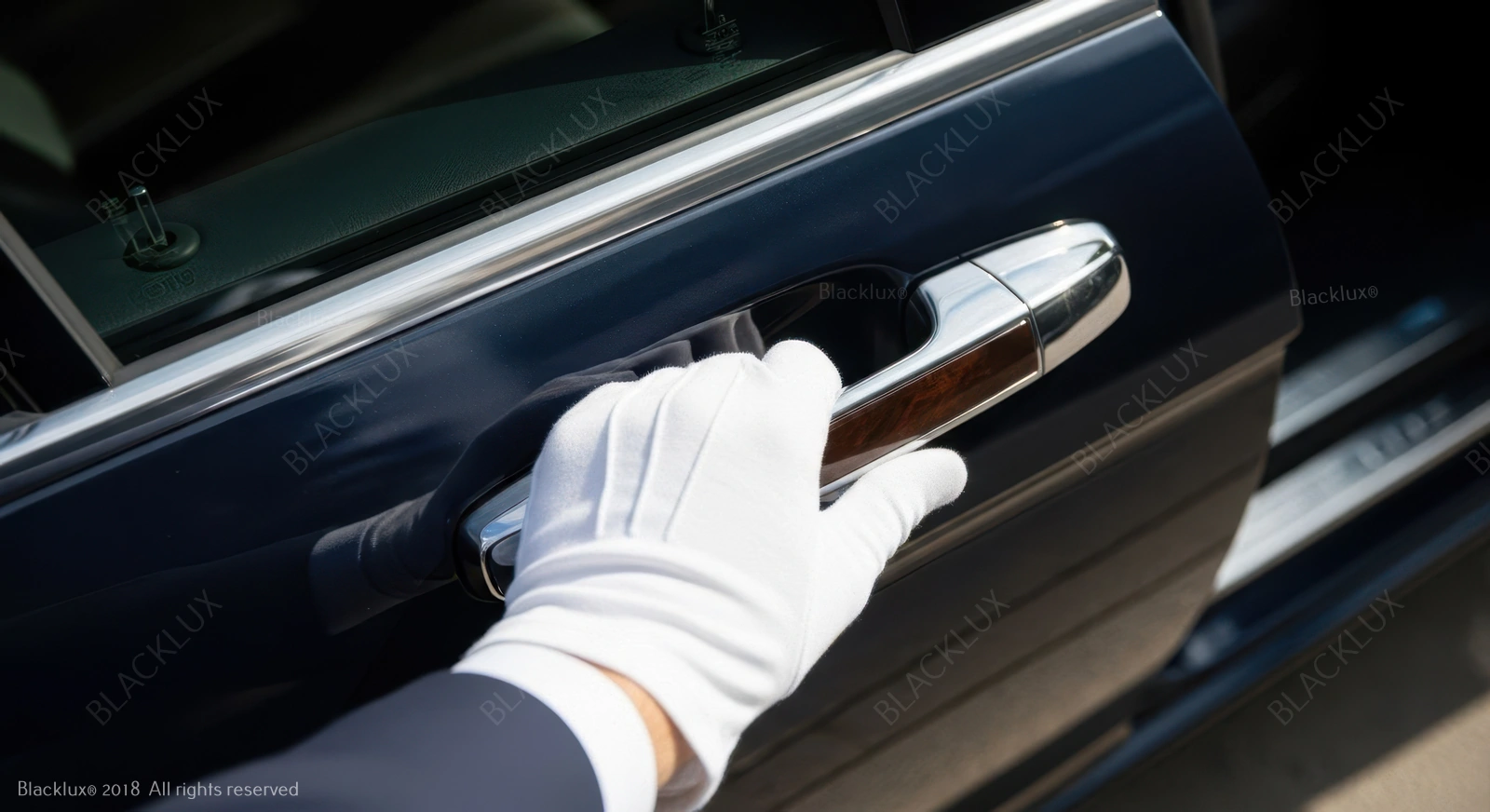 White-gloved hand holding the chrome exterior handle of a black car door