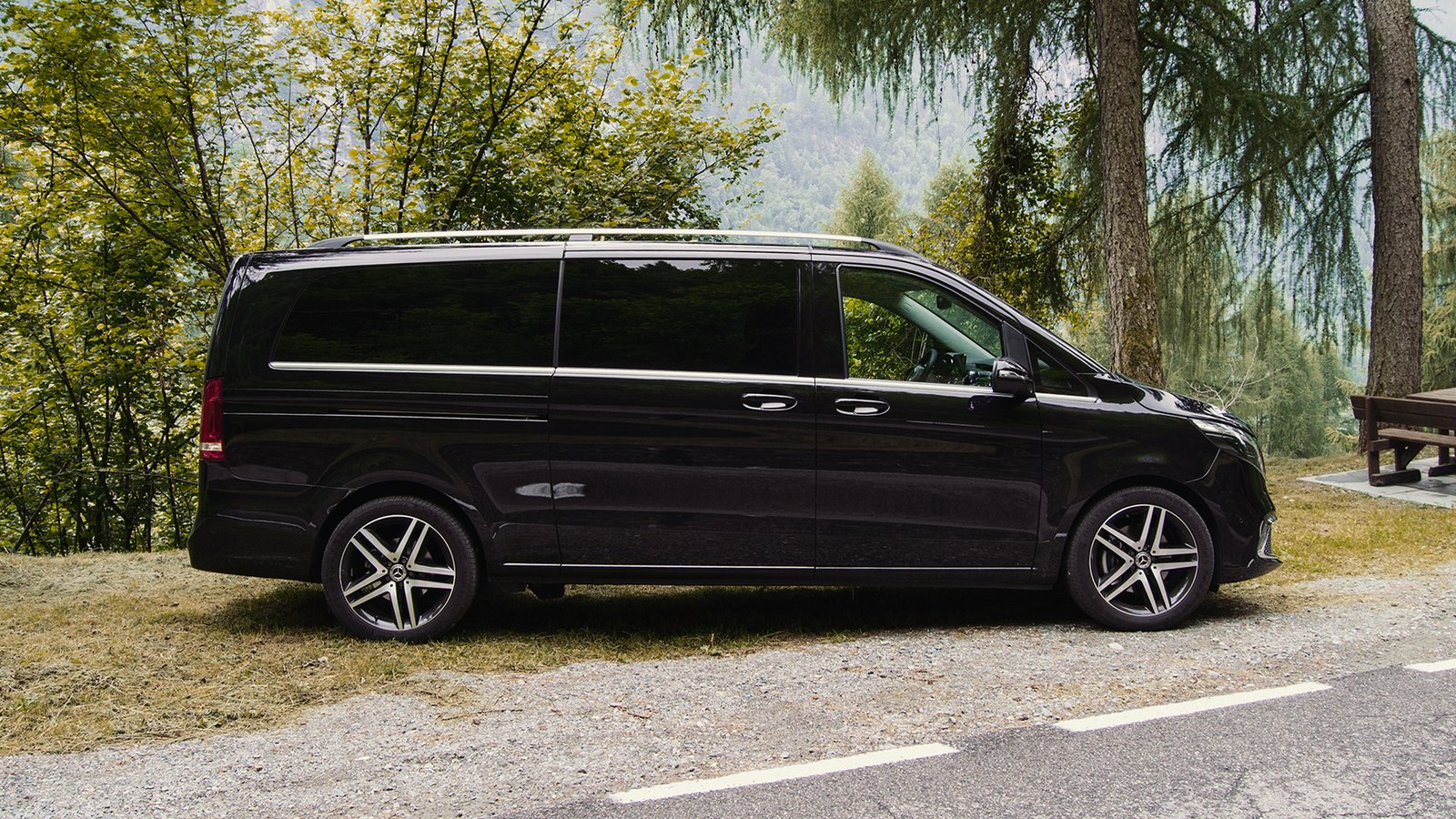 Side view of a black passenger van beside a wooded road