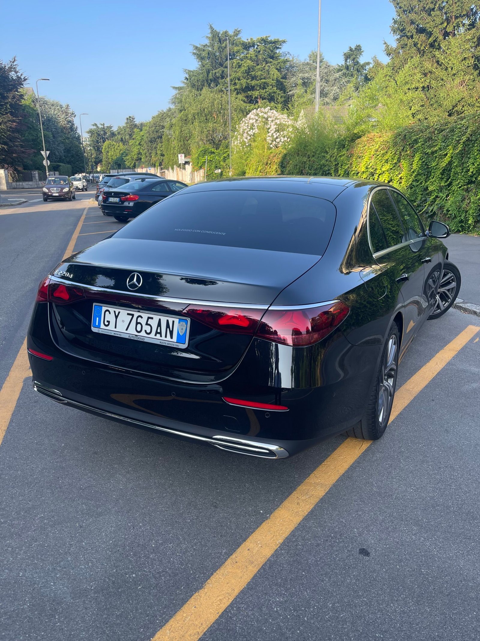 Rear view of a black saloon parked beside a tree-lined road
