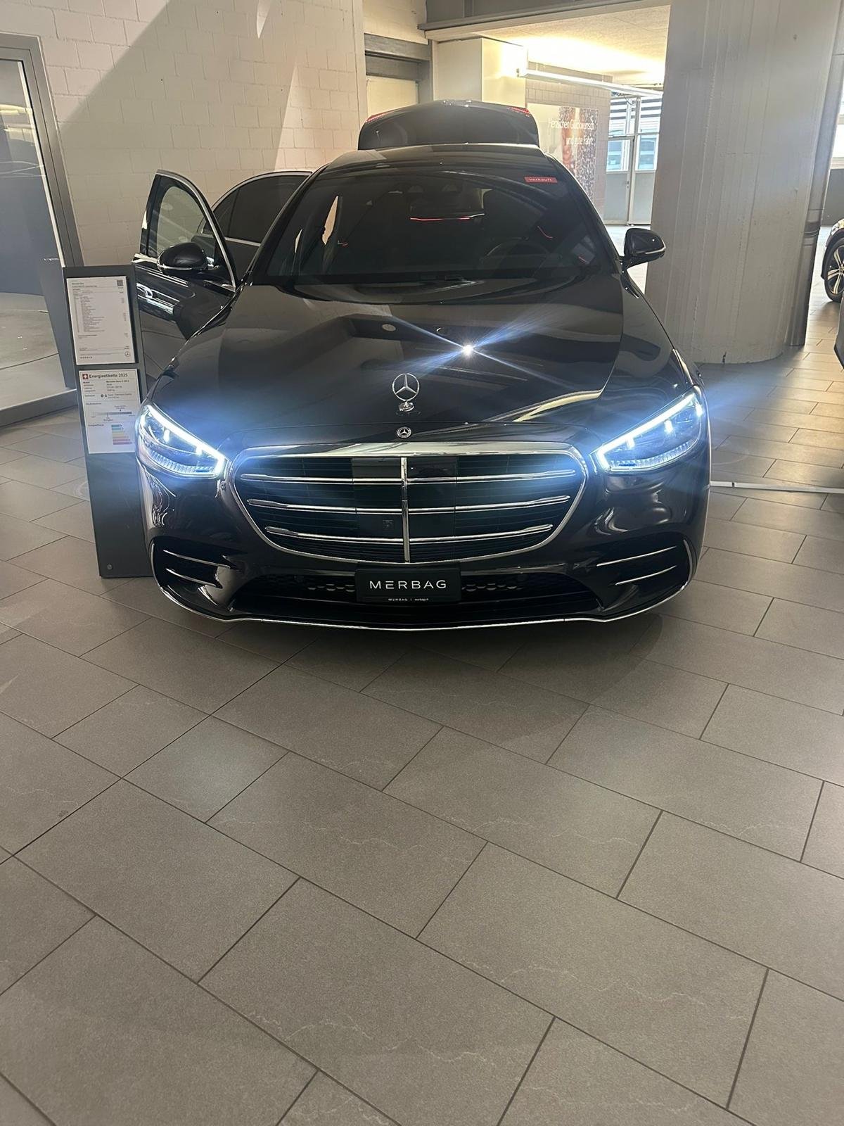 Black saloon with headlights on and both front doors open in a showroom