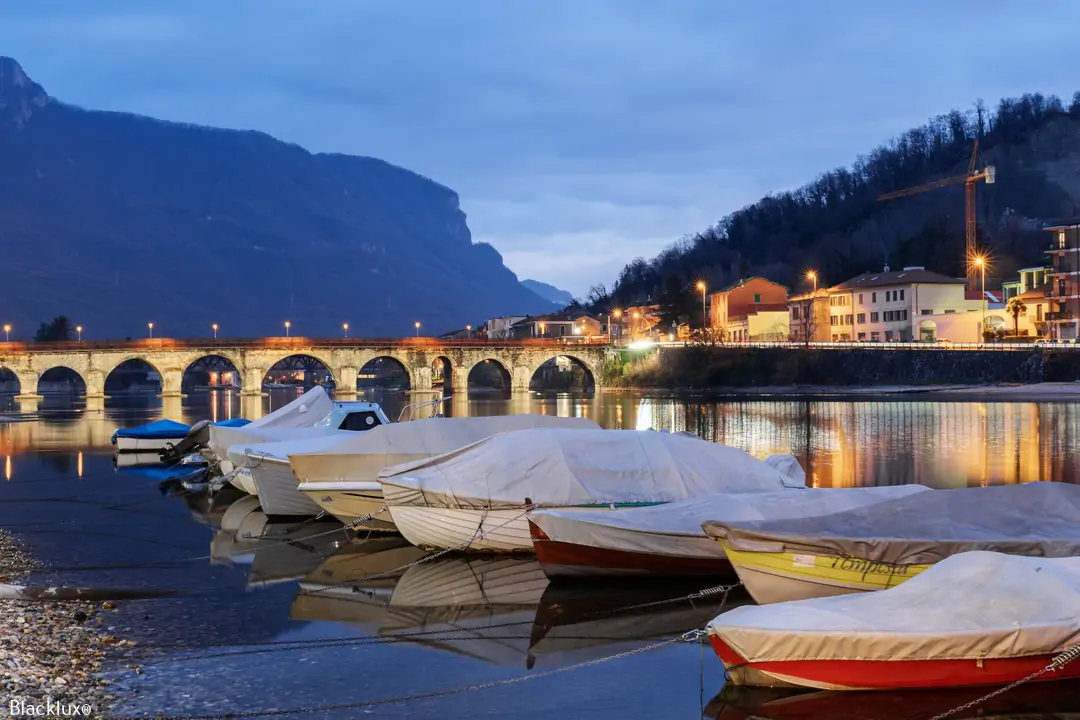 Small covered boats beside a waterfront with an illuminated arched bridge