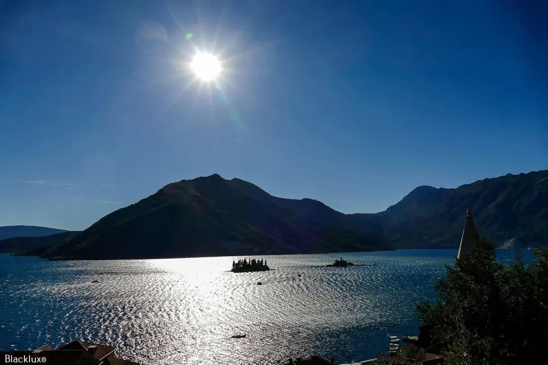 Bright sun reflected on a lake with dark hills and small boats