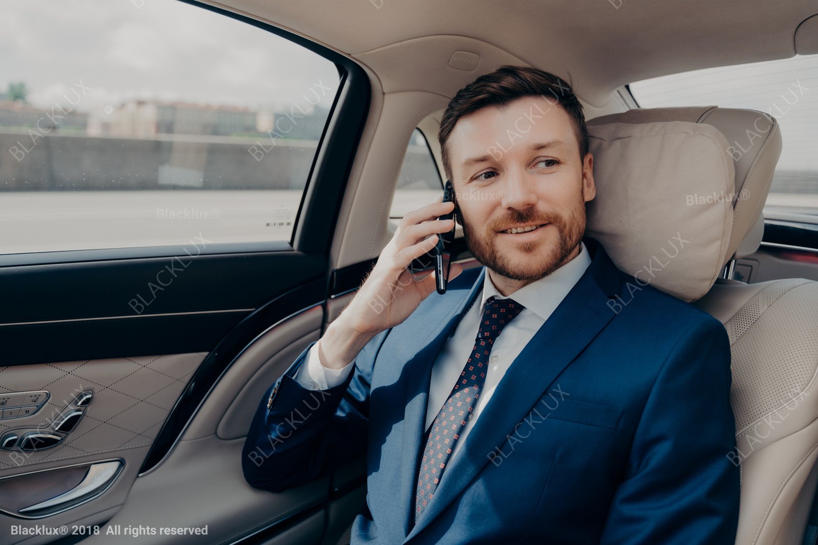 Passenger in a blue suit making a phone call from a light-coloured rear seat