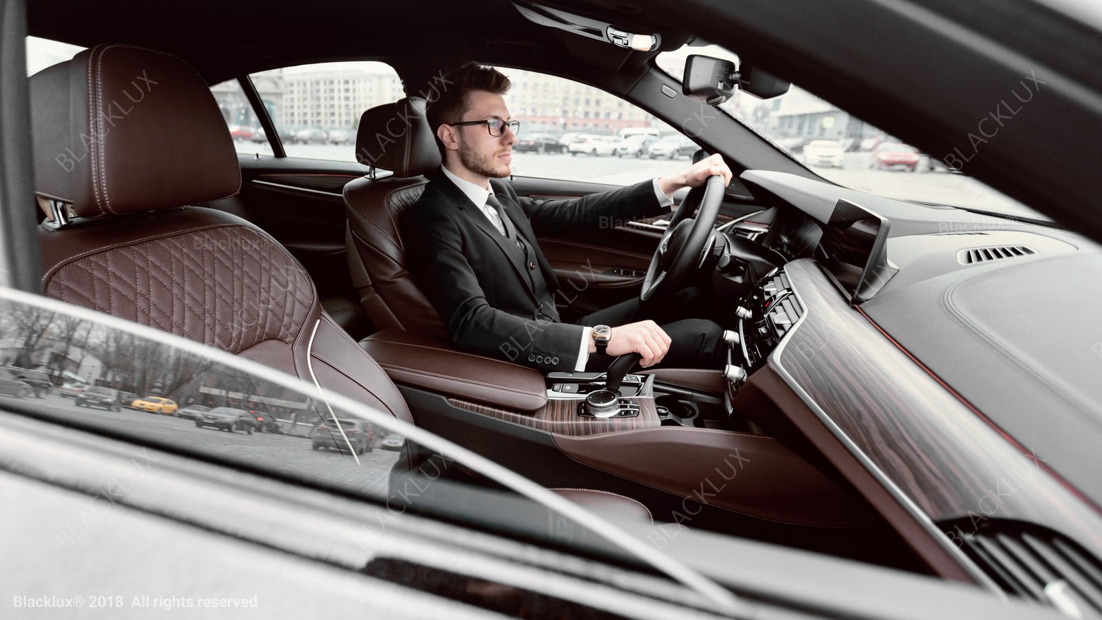 Driver in a dark suit seen across a brown-leather front cabin in daylight