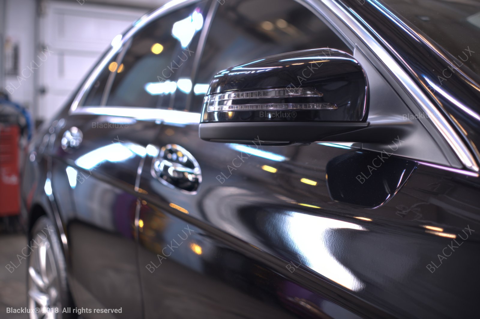 Close view of a glossy black vehicle side mirror, window trim and reflected lights