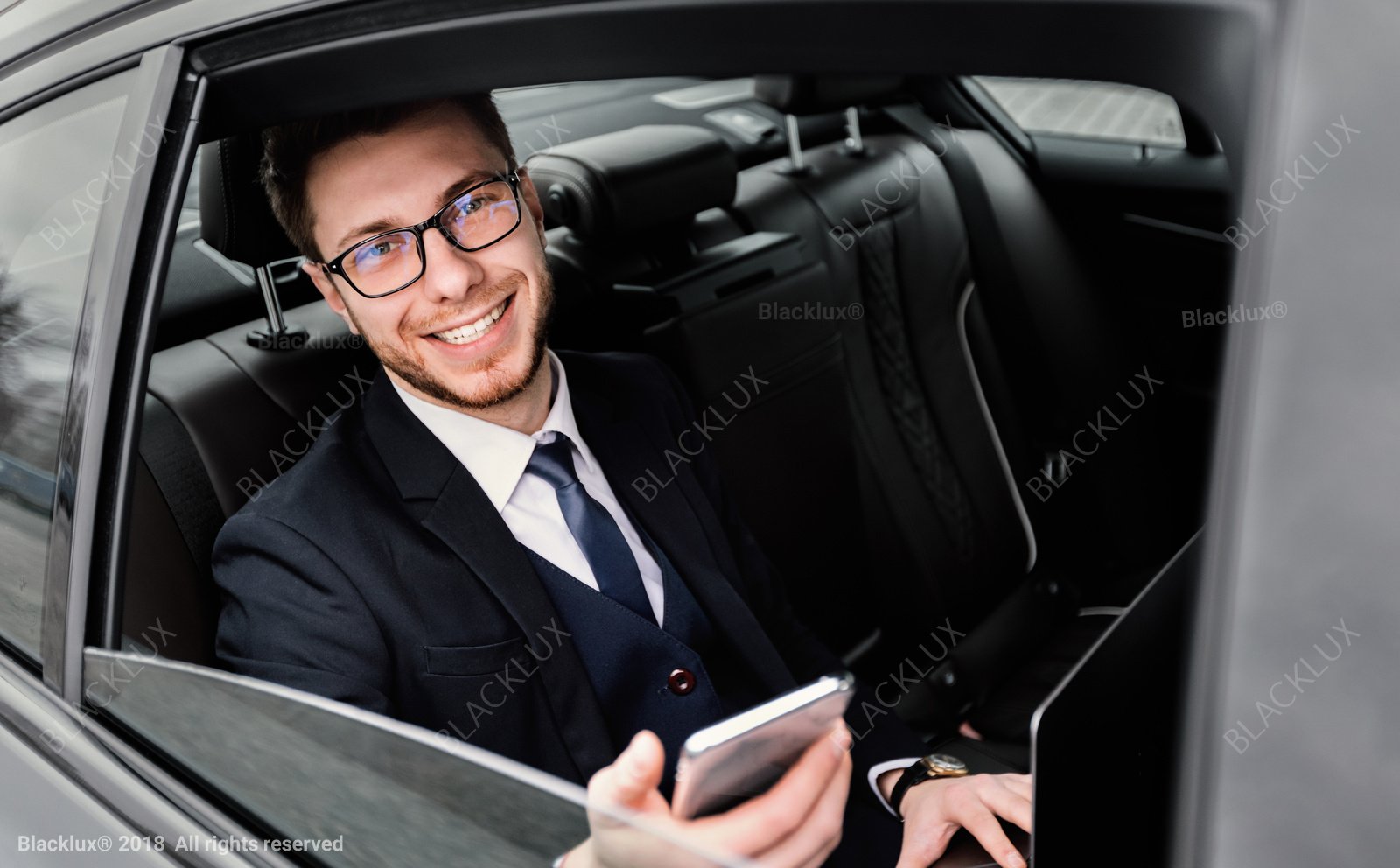 Business traveller with glasses and a smartphone seated beside an open car window