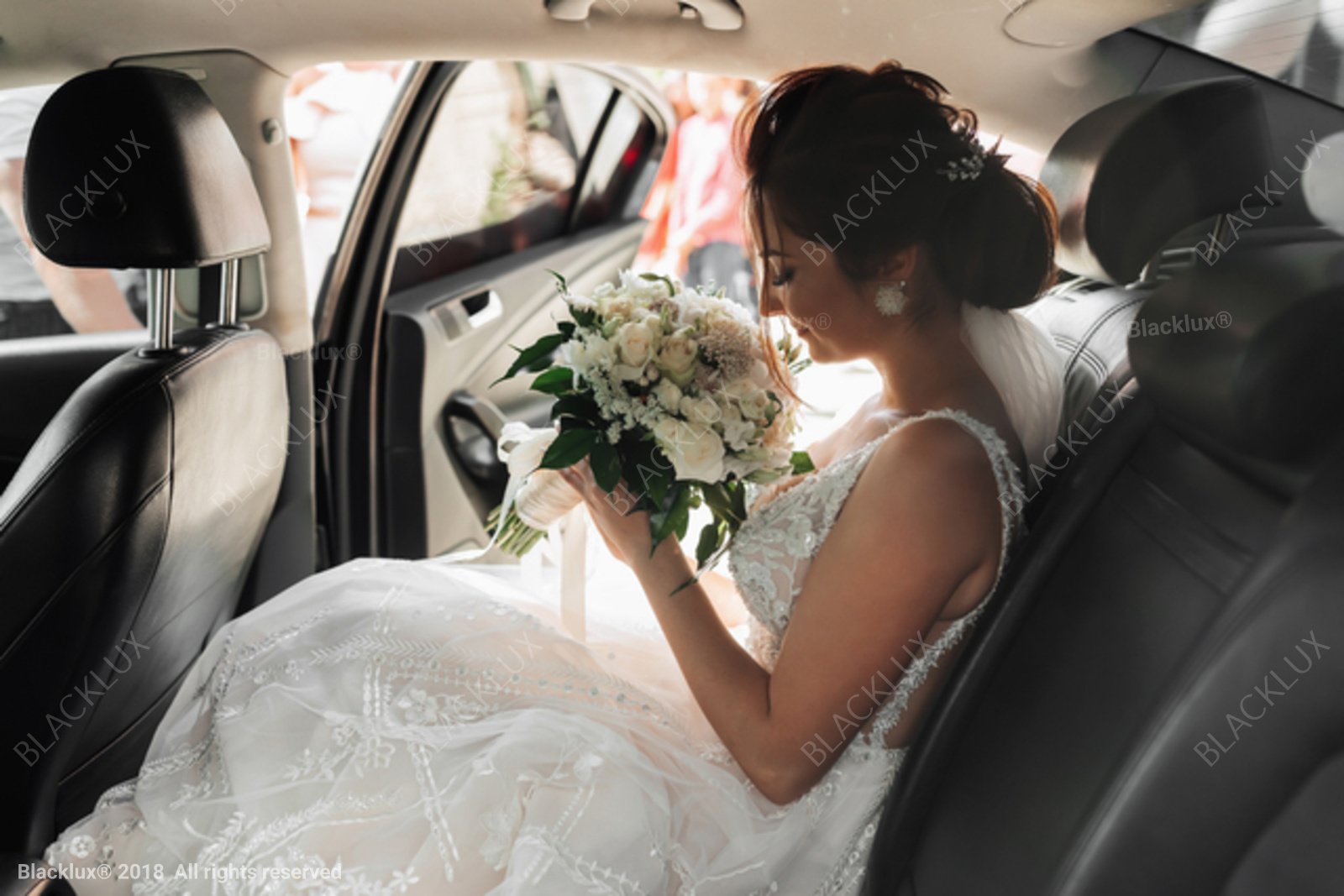Bride holding a bouquet of white flowers while seated inside a car