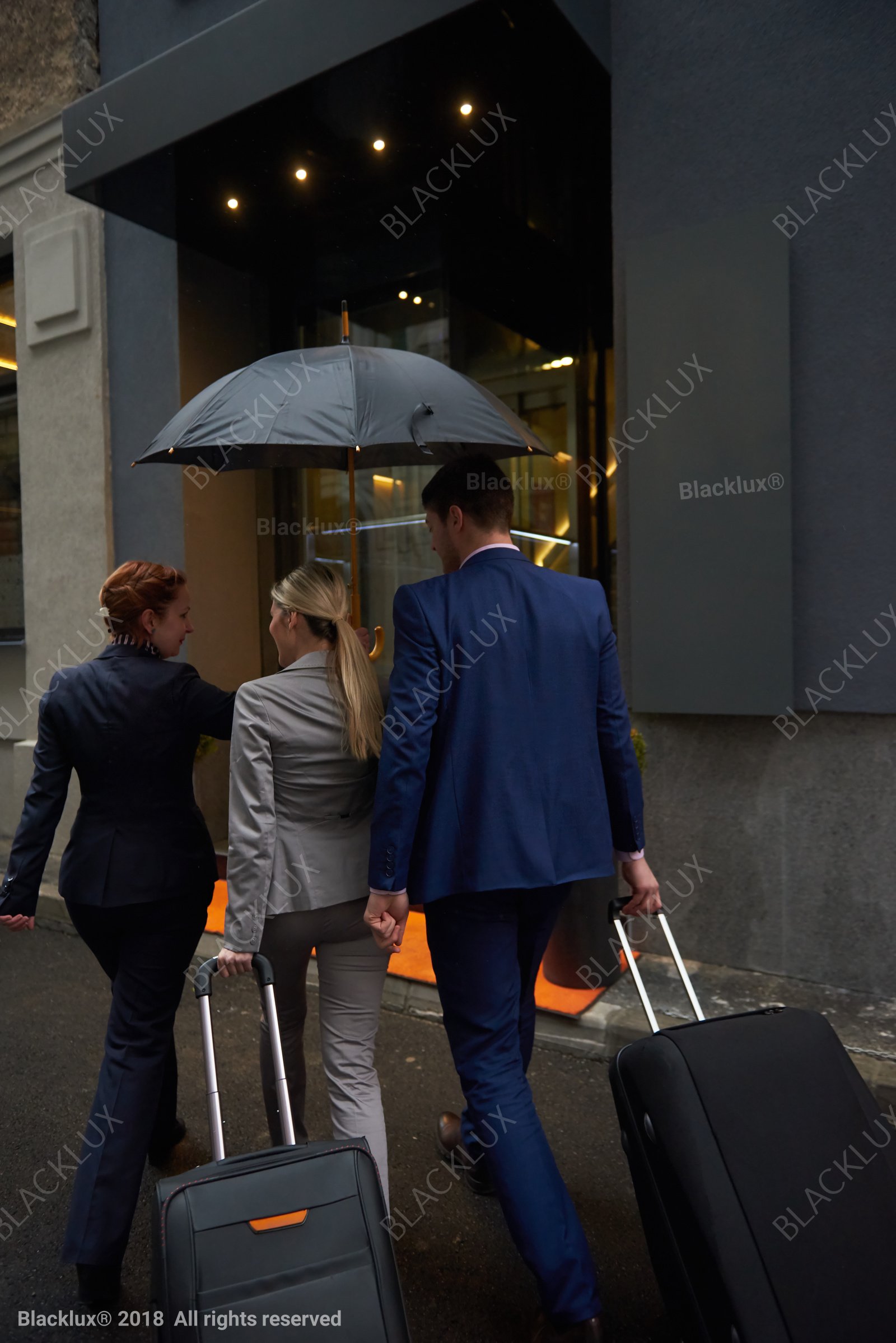 Two business travellers approaching a hotel entrance beneath an umbrella