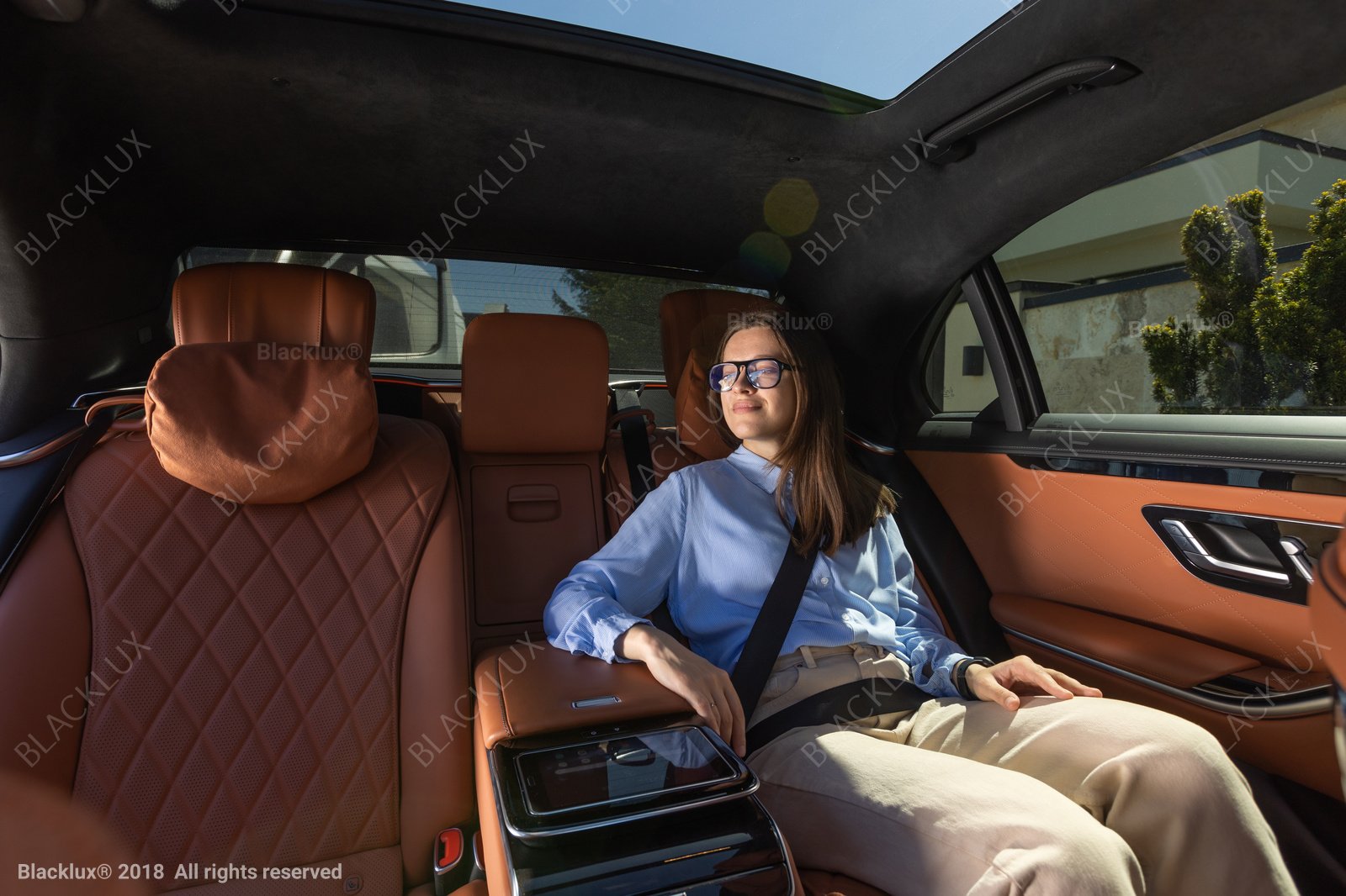 Passenger wearing a seat belt in a cognac-coloured rear cabin with daylight through a panoramic roof