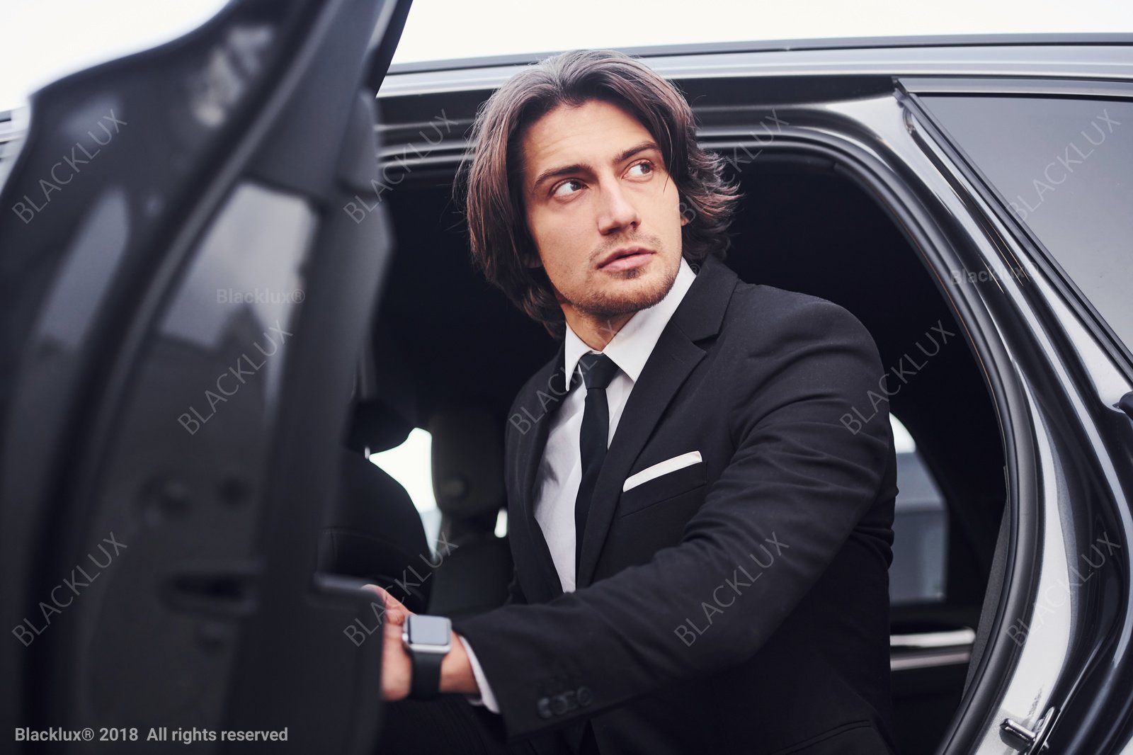 Man in a dark suit looking upward while stepping out of a dark car