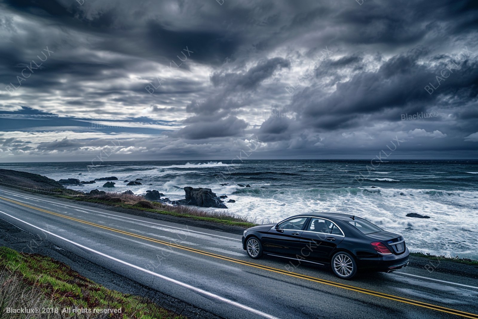 Dark coastal-road scene with a car beside the sea beneath a dramatic cloudy sky