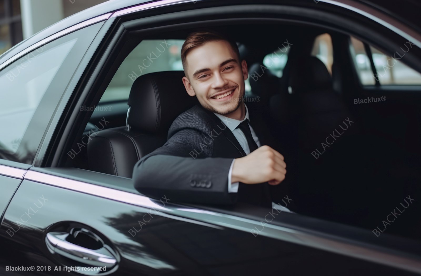 Smiling passenger in a dark suit beside the open rear window of a black car
