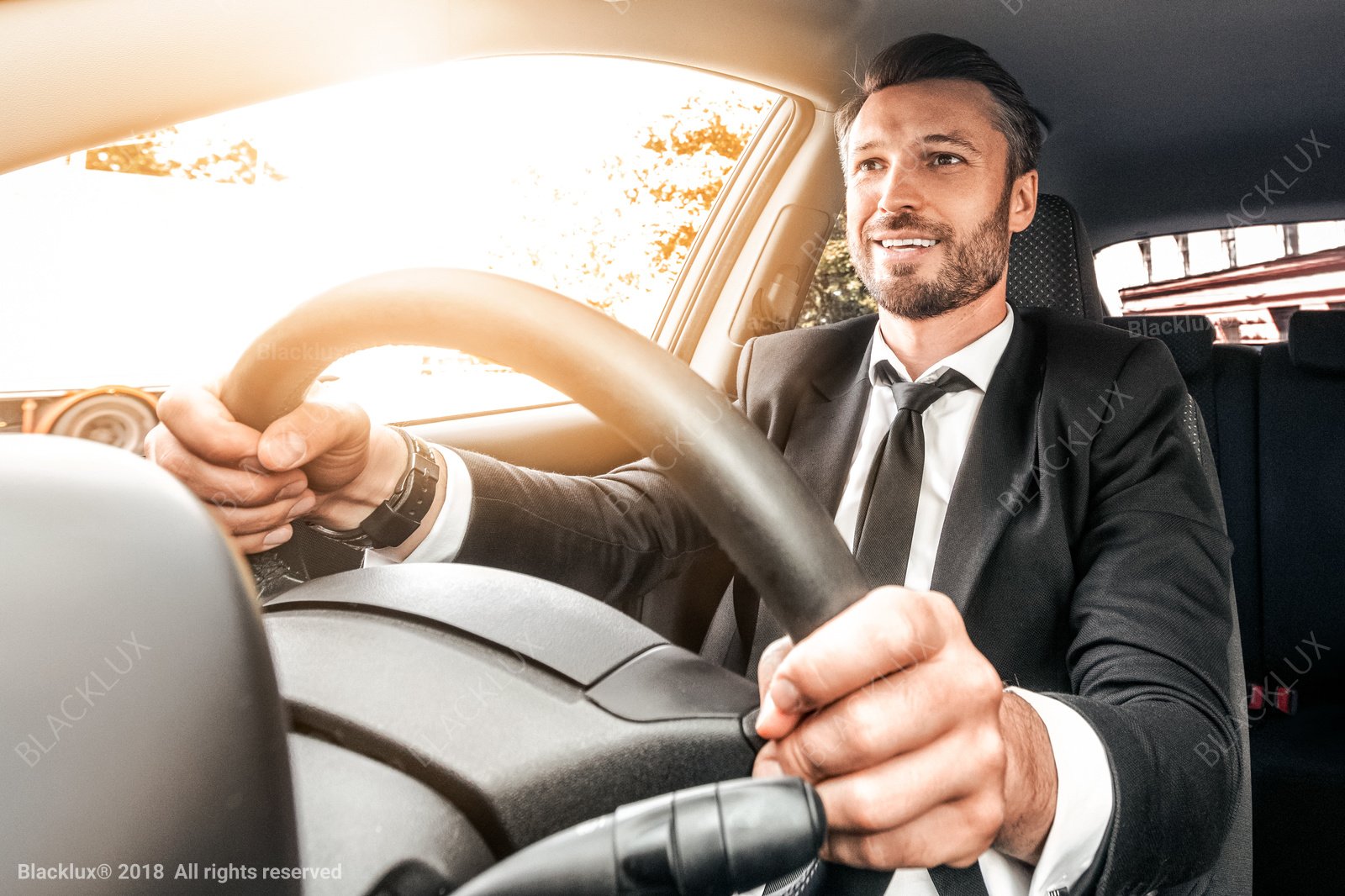 Man in a dark suit holding a steering wheel in warm daylight