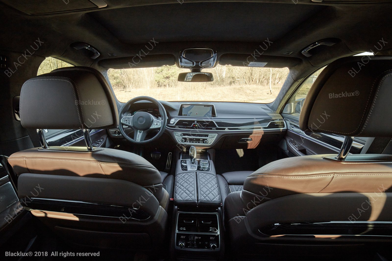 View from the rear of a vehicle toward brown front seatbacks and a central dashboard in daylight