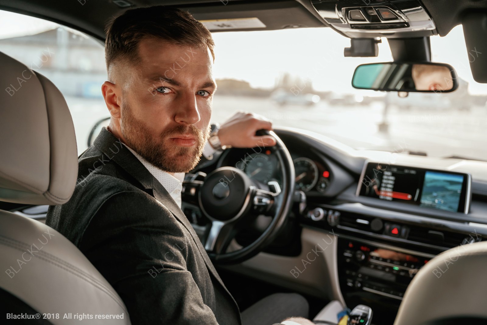 Suited driver in the front seat turning towards the rear cabin in daylight