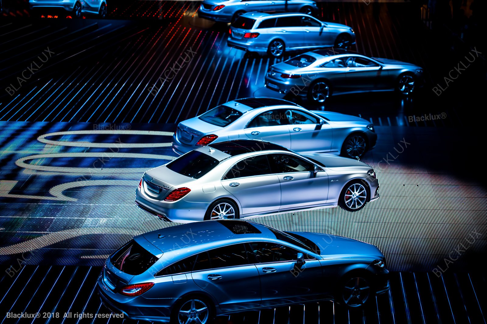 Elevated view of several cars displayed in diagonal rows under blue exhibition lighting