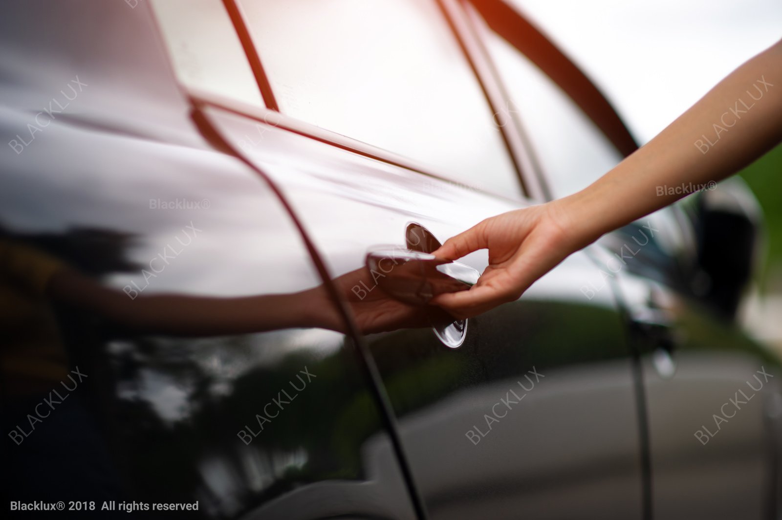 Close-up of a hand opening the exterior door handle of a polished black car in daylight
